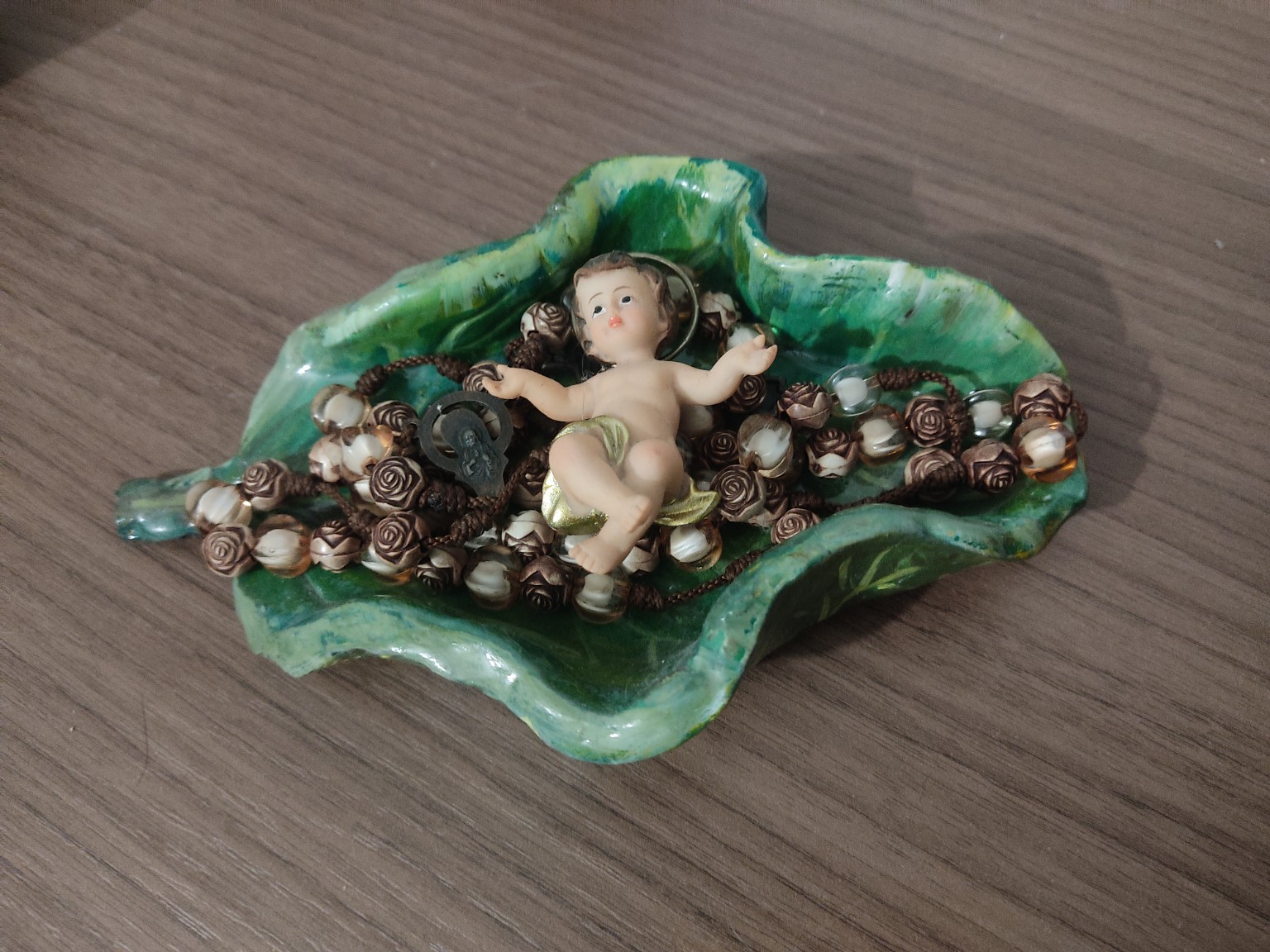 Hoja de cerámica sosteniendo rosarios y una figura del Niño Jesús